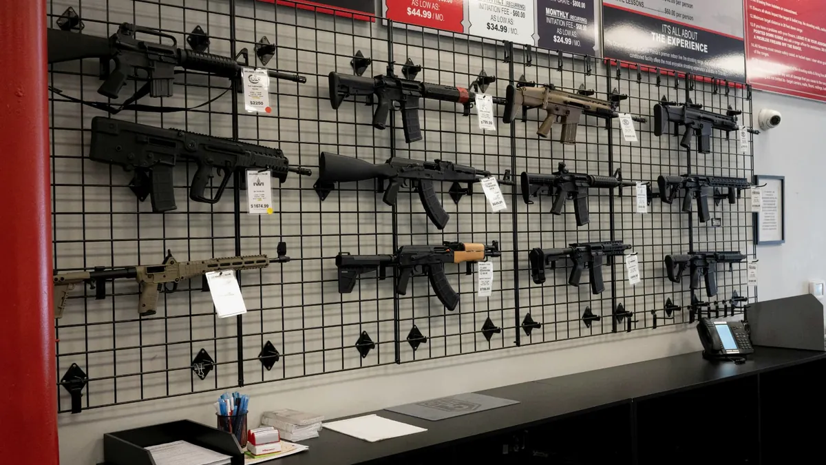 Interior de loja especializada com armas longas expostas em painel e balcão de atendimento